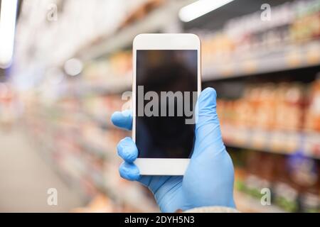 Gros plan de la femme dans des gants de protection tenant le téléphone mobile et faire une photo dans un supermarché Banque D'Images