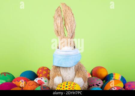 figurine de lapin avec masque facial entre les œufs de pâques peints avant le fond de gren, symbole de l'impact du virus corona sur la saison de pâques Banque D'Images