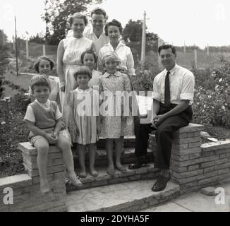 Dans les années 1950, historique, dans un jardin à l'arrière, deux familles se tiennent sur les marches pour une photo de groupe Angleterre, Royaume-Uni. La Grande-Bretagne d'après-guerre a été un âge plus innocent moins compliqué, où les femmes avaient l'air élégantes et les enfants avaient l'air, bien des enfants. Banque D'Images