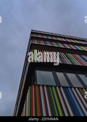Vue à angle bas d'un immeuble résidentiel moderne avec balustrade de balcons multicolores et fenêtres sur la façade par temps nuageux.