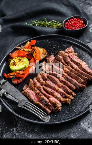 Rouleau en tranches de Chuck Eye sur une assiette avec un plat de légumes. Arrière-plan noir. Vue de dessus Banque D'Images