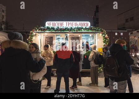 Saint-Pétersbourg, Russie - 26 décembre 2020 : les jeunes se tiennent en ligne pour la pâtisserie tchèque (trdelniks) dans une rue du port nocturne de Sevkabel. Banque D'Images