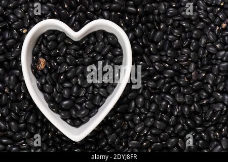 Haricots noirs dans un fond et une texture de bol en forme de coeur. Vue de dessus. Banque D'Images