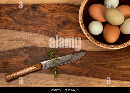 un fond de cuisine avec un bol d'œufs colorés sur une planche à découper avec un couteau fait main. Le coin supérieur gauche est ouvert pour le texte. Banque D'Images