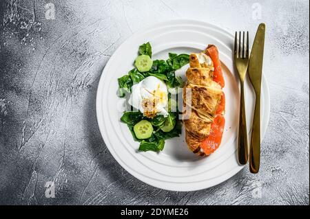 Sandwich croissant au saumon salé servi avec des feuilles de salade fraîches, des épinards, des œufs et des légumes. Arrière-plan gris. Vue de dessus Banque D'Images