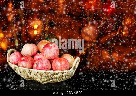 Pommes rouges mûres dans un panier en osier sur un flou Arrière-plan de Noël Banque D'Images