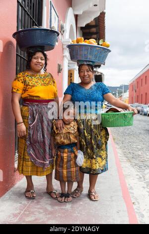 Antigua, Guatemala les femmes portant des paniers de fruits sur leur tête posent avec une fille Banque D'Images