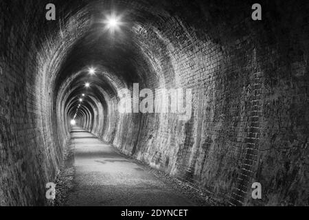 Un vieux tunnel en briques, éclairé par un éclairage électrique. Noir et blanc. Photographié dans l'ancien tunnel ferroviaire de la gorge de Karangahake, Nouvelle-Zélande Banque D'Images