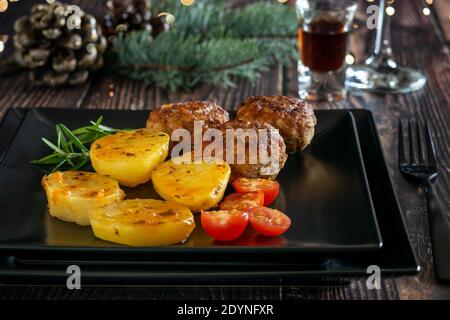Boulettes de viande frites avec pomme de terre et petite cerise de tomate sur le plat moderne noir, préparé pour le dîner de fête.Noël décoration maison, lumières et b Banque D'Images