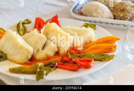 Tranches de morue chaude frite avec des tranches de poivrons doux sur le plat blanc. Une assiette avec des petits pains sur la table de service. Fruits de mer sains de mediterran Banque D'Images