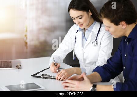 Une jeune femme-médecin sympathique écoute sa patiente, tout en étant assise dans une clinique ensoleillée. Concepts de médecine et de soins de santé Banque D'Images