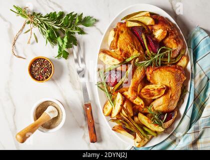 pommes de terre rôties, betteraves, haricots verts et pattes de poulet servies sur une plaque ovale blanche sur une table en marbre avec épices et romarin, vue horizontale de l'ab Banque D'Images
