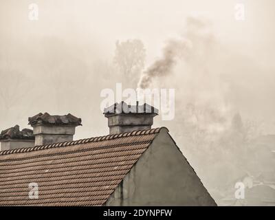 Paysage rural avec la fumée qui s'élève de la cheminée d'un maison avec vieux toit en tuiles rouges Banque D'Images