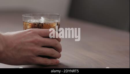 homme à la main prendre le cola dans verre à verre avec glace de table en noyer avec espace de copie, photo large Banque D'Images