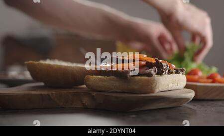 L'homme a mis des tranches de steak sur un petit pain de ciabatta pour un sandwich sur le comptoir de la cuisine, photo large Banque D'Images