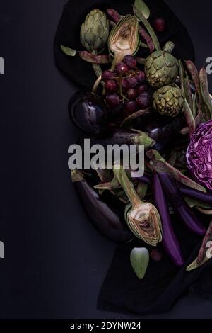 Artichauts violets, aubergines, raisins et haricots sur fond sombre avec espace de copie gauche. Banque D'Images