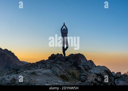 Un touriste faisant du yoga sur le point culminant de la montagne rocheuse Regarder le soleil se lever dans la vallée du Darband en automne à l'aube Contre le ciel coloré dans la montagne Tochal Banque D'Images