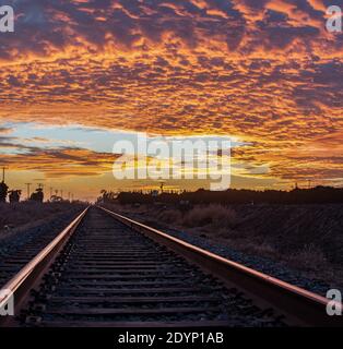 Les voies ferrées de la raillode rurale convergent à la distance où l'horizon rencontre les nuages colorés vibrants du ciel. Banque D'Images