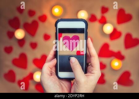 Mains de femmes tenant un téléphone mobile prenant une photo de coeur romantique rose de la Saint-Valentin . Carte de vœux pour la Saint-Valentin, vue de dessus, arrière-plan romantique Banque D'Images