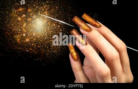 Main avec une manucure or et une brosse sur un fond noir recouvert de sparkles. Forme des ongles. Clous étendus. Banque D'Images