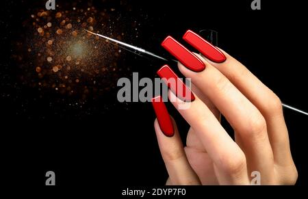 Main avec une manucure rouge et une brosse sur un fond noir parsemé de sparkles. Forme des ongles. Clous étendus. Banque D'Images