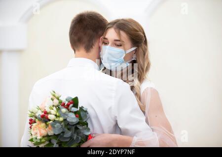 La mariée dans un masque médical avec un bouquet de fleurs danse avec le marié. Mariage pendant le coronavirus panademia. Banque D'Images