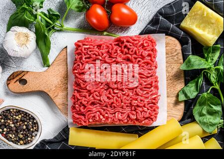 Le concept de la cuisson des pâtes cannelloni avec du bœuf haché. Ingrédients basilic, tomates cerises, parmesan, ail. Arrière-plan gris. Vue du dessus Banque D'Images
