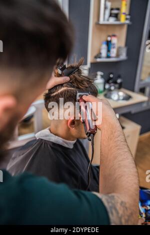 Barber coupe les cheveux à son jeune client avec sa tondeuse Banque D'Images