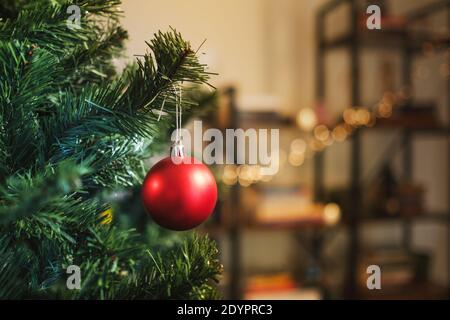 Décoration de noël sphérique suspendue sur une branche d'un arbre de noël dans une pièce avec une étagère de livre défocused sur le fond. Banque D'Images