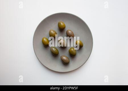 Olives vertes sur plaque en béton gris isolée sur fond blanc d'une vue en grand angle Banque D'Images