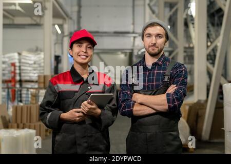 Deux jeunes ingénieurs à succès de grande usine contemporaine allée entre les piles de matières premières emballées dans l'entrepôt Banque D'Images