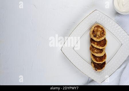 Cheesecakes sur une assiette blanche. À côté des cheesecakes se trouve une tasse de crème aigre et une cuillère. Vue de dessus. Gros plan. Photographie macro Banque D'Images