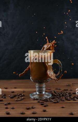 Éclaboussures de café dans une tasse en verre sur fond sombre. Banque D'Images