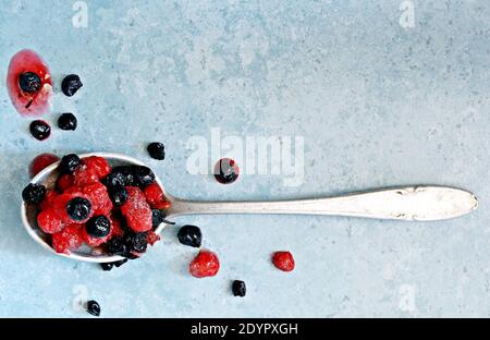 Cerises congelées (décongelées), bleuets, raisins de Corinthe rouges dans une cuillère sur fond bleu. Fruits sains, préparations faites maison pour préparer des smoothies, compo Banque D'Images