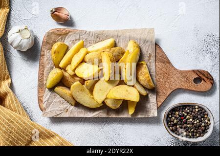 Frites surgelées, quartiers de pommes de terre sur une planche à découper en bois. Arrière-plan blanc. Vue de dessus Banque D'Images