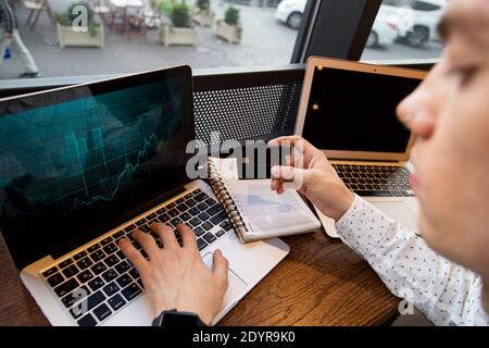 Un homme réussi met des Paris sur la bourse. Concept de littératie financière. Investissements de marché. Le jeune homme est assis dans une maison de café avec ses ordinateurs portables et Banque D'Images