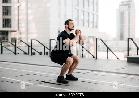 FIT homme entraînement air squat exercice. Posez un homme exerçant crossfit à l'extérieur. Jeune beau mannequin de fitness caucasien mâle et instructeur à l'extérieur. Noir Banque D'Images