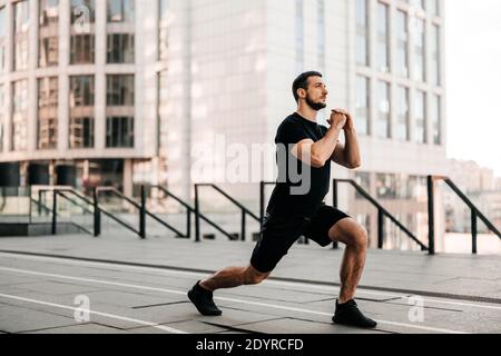 Faites avancer l'homme qui fait une fente. Le sport dans le concept de la grande ville. Homme fort qui étire les jambes avant de faire du jogging. Concept de soins de santé. Coureur de sport noir Banque D'Images