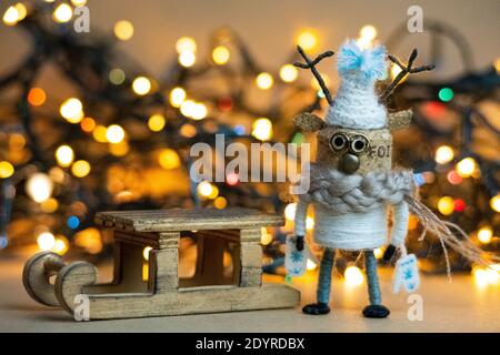 Renne en liège habillé pour l'hiver avec un traîneau devant le bokeh chaud des lumières de Noël Banque D'Images