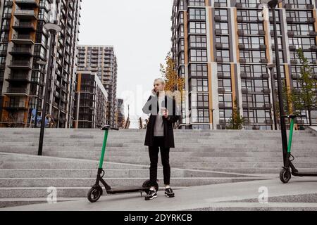 Guy louait un scooter. Automne dans la grande ville. Homme dans des vêtements décontractés discute des termes de location de scooter par son téléphone. Appartements sur fond Banque D'Images