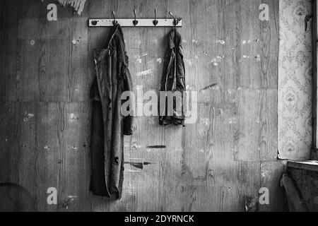 Une photo en niveaux de gris de vêtements suspendus sur un mur sale d'une pièce abandonnée Banque D'Images