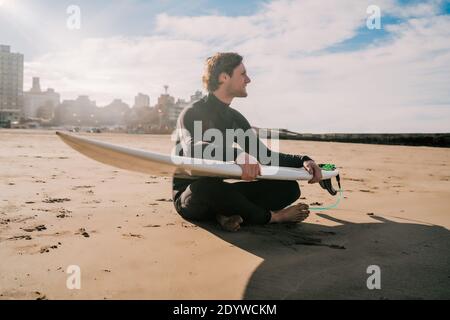 Surfeur assis sur une plage de sable avec planche de surf. Banque D'Images