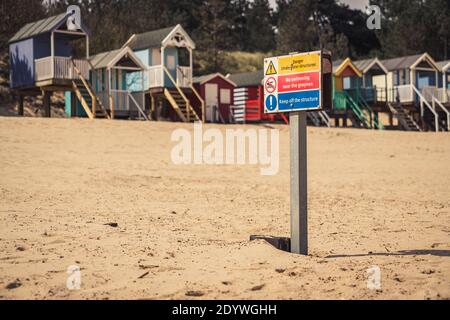 Signer : Danger Les structures sous-marines, pas de piscine à proximité de l'épis, Garder hors de la structure - avec des cabines de plage à l'arrière-plan flou, vu dans les puits-nex Banque D'Images