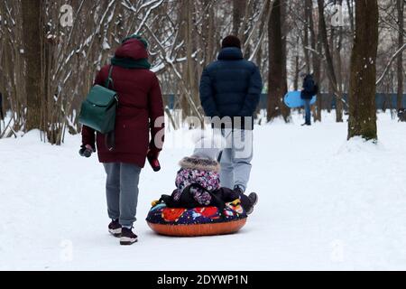 Loisirs en famille dans le parc d'hiver, parents et un enfant sur le tube de neige. Les gens qui marchent par temps froid Banque D'Images