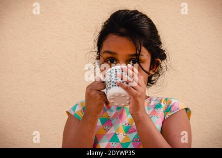 Un jeune enfant qui va à l'école l'apprécie et la boit lait chaud dans une tasse Banque D'Images