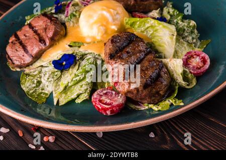 Œufs benedict avec viande de boeuf sur une grande assiette blanche. Petit-déjeuner anglais traditionnel avec œufs Benedict, tomates cerises et laitue. Œuf Benedict servi Banque D'Images