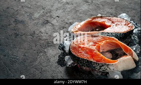 Deux steaks de saumon sauvage crus sur glace sur fond noir texturé. Steaks de saumon avec espace de copie laissé. Bannière horizontale Banque D'Images