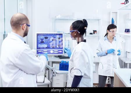Un scientifique et un collègue africain discutant de leurs recherches sur le virus dans un laboratoire occupé. Une équipe multiethnique de chercheurs médicaux travaillant ensemble dans un laboratoire stérile portant des lunettes et des gants de protection. Banque D'Images