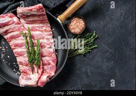 Râtelier de côtes de porc crues non cuites assaisonnées d'épices dans une casserole. Arrière-plan noir. Vue de dessus. Copier l'espace Banque D'Images