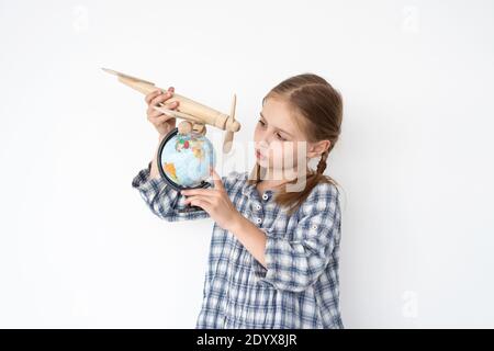 Jolie petite fille volante avion en bois sur le globe sur blanc arrière-plan de la paroi Banque D'Images